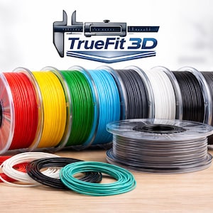 May include: A collection of colorful 3D printer filament spools in red, yellow, green, blue, black, white, and gray. The spools are arranged on a wooden surface with the "TrueFit 3D" logo in the background. Several loose coils of filament are also visible.