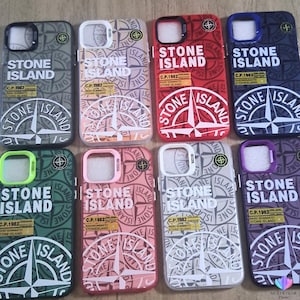 Peut inclure: Huit coques de smartphone de différentes couleurs, chacune arborant le logo Stone Island, un graphique de boussole et le texte C.P. 1982 RASO GOMMATO STONE ISLAND. Les coques sont disposées sur deux rangées, présentant des coloris distincts dont gris, rouge, bleu, vert et rose.