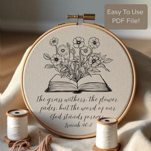 Könnte beinhalten: Ein Stickrahmen mit einem Blumen- und Buchdesign. Die Schwarz-Weiß-Illustration zeigt Blumen, die aus einem offenen Buch hervorgehen. Der Text lautet: "Das Gras verdorrt, die Blume verwelkt, aber das Wort unseres Gottes bleibt ewiglich. Jesaja 40,8".