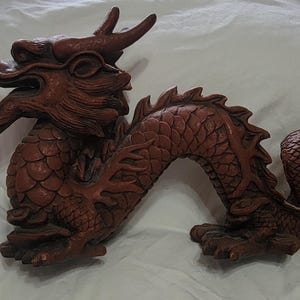 May include: A reddish-brown dragon figurine featuring intricate scale textures, a long serpentine body, and a detailed head with an open mouth showing teeth. The creature is depicted in a coiled, dynamic pose with visible claws and horns.