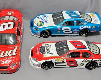 May include: Three die-cast stock car models featuring the number 8. One is red with Budweiser branding. Another is blue with Oreo and Ritz logos. The third is red and white with Budweiser, Oreo, and Ritz branding. All feature sponsor decals.