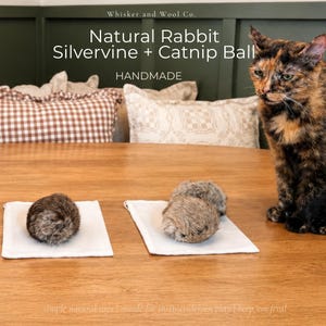 May include: Three round, fuzzy, brown rabbit fur balls for cats, displayed on small white fabric squares. The text reads: Whisker and Wool Co. Natural Rabbit Silvervine + Catnip Ball HANDMADE. simple natural toys | made for instinct-driven play | keep 'em feral