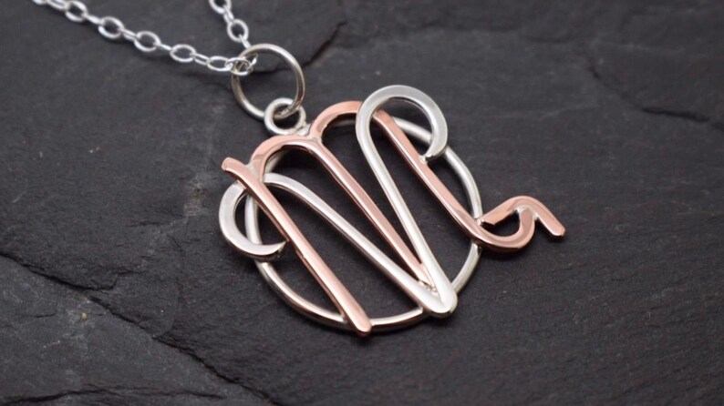 May include: A silver necklace with a rose gold Virgo zodiac sign pendant. The pendant is a circle with the Virgo symbol inside.