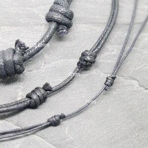 May include: Three black cords of different thicknesses, 1mm, 2mm, and 3.5mm, are shown knotted together. The cords are on a gray textured surface.
