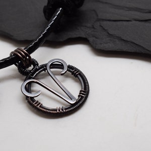 May include: A black leather cord bracelet with a silver wire-wrapped pendant featuring the astrological symbol for Aries.