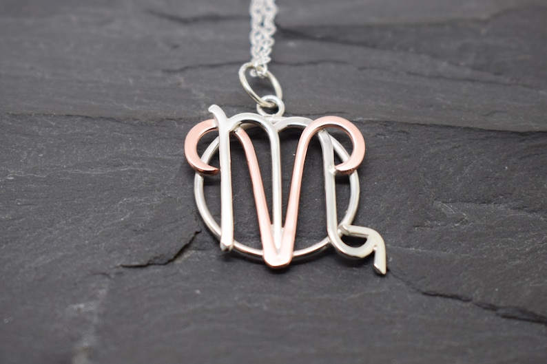May include: A silver and rose gold necklace with a zodiac pendant featuring the symbol for Aries.