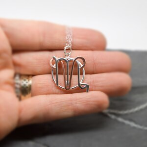 May include: A silver necklace with a Virgo zodiac sign pendant. The pendant is a delicate, open-work design.