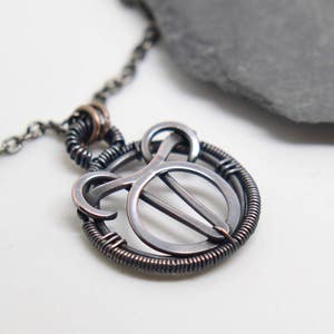 May include: A handcrafted silver-toned pendant necklace with a distinctive, abstract design. The pendant has a circular frame with wire wrapping and an inner design. The necklace chain is also silver-toned.