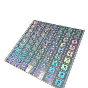 May include: A sheet of holographic stickers featuring the PlayStation logo and the word "SONY". The stickers have a square shape with a reflective, iridescent finish, displaying a range of colours. The sheet is rectangular with a white background.