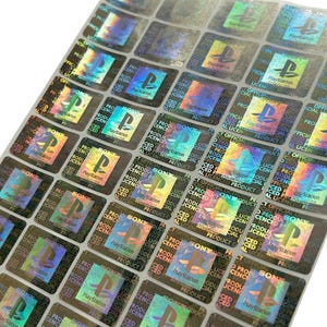 Pode incluir: Folha de autocolantes holográficos de autenticação de produtos PlayStation. Cada autocolante quadrado apresenta o logótipo PlayStation, as palavras "PlayStation" e "OFFICIAL LICENSED PRODUCT."
