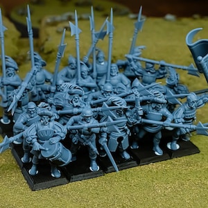 May include: A group of miniature figurines of soldiers, painted in a muted blue-gray color. The soldiers are armed with spears, swords, and halberds, and are arranged on a black base. One figure is playing a drum. The scene is set on a green surface.