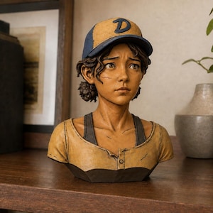 May include: A sculpted bust of a young person with brown hair, wearing a blue and tan baseball cap with a letter D on the front. The figure has a tan shirt with a dark gray collar and trim, featuring visible scratch marks on the skin and clothing.
