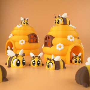 Op de afbeelding: Een verzameling gele en bruine bijenbeeldjes en bijpassende bijenkorfvormige huizen. De bijenkorven hebben bruine boogvensters en witte bloemaccenten. De bijen hebben witte vleugels en staan in verschillende poses.