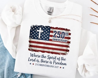 May include: White sweatshirt with a distressed American flag design, a cross, and the text "250th Anniversary." The phrase "Where the Spirit of the Lord is, there is Freedom" is printed on the shirt. The text "2 Corinthians 3:17" is also printed on the shirt.