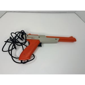 May include: An orange and grey Nintendo Zapper light gun with a black cord. The gun has a ribbed handle and the Nintendo logo is visible. A classic video game accessory.