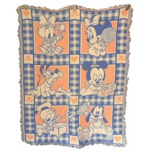 Puede incluir: Una manta de bebé vintage con un diseño de cuadros vichy azul y melocotón. La manta presenta los personajes de dibujos animados Daisy Duck, Minnie Mouse, Pluto, Mickey Mouse, Donald Duck y Goofy. Tiene un borde con volantes.