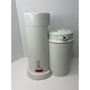 May include: White Mr. Coffee Iced Tea Pot with a tall, cylindrical body and a smaller, rounded pitcher. The text "THE ICED TEA POT BY MR. COFFEE" is printed in red on the front of the tall pot. A red accent band is on the pitcher.