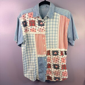 Peut inclure: Une chemise à manches courtes boutonnée présentant un motif patchwork composé de denim bleu clair, de vichy blanc et bleu, et de panneaux de tissu floral avec des motifs de cœurs rouges. La chemise inclut des bordures en dentelle blanche.