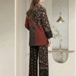Könnte beinhalten: Eine langärmelige Tunika und eine passende Hose mit weitem Bein im Patchwork-Design aus schwarzem und rostfarbenem Stoff mit komplizierten Blumen- und geometrischen Mustern. Das Set zeigt eine Mischung aus dunklen Blumendrucken und einfarbigen Bahnen.
