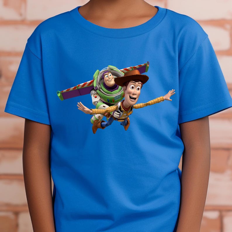 May include: A blue t-shirt featuring a graphic of Woody and Buzz Lightyear from Toy Story. Woody is wearing a cowboy hat and Buzz is in his spacesuit. The characters are depicted mid-air, with Buzz's wings extended.