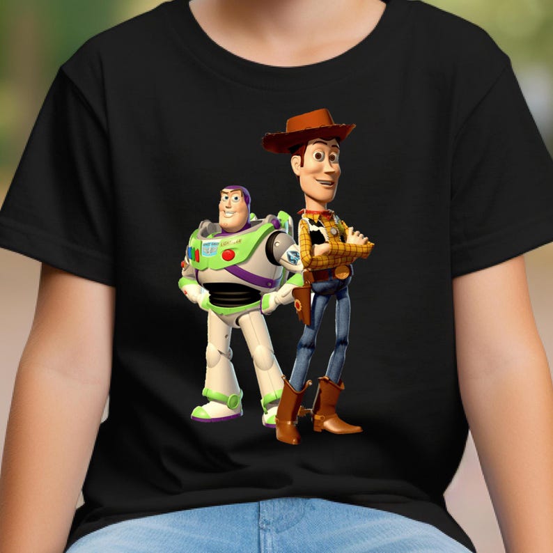 May include: A black short-sleeved t-shirt featuring a graphic print of the characters Buzz Lightyear and Woody from Toy Story. Buzz Lightyear is depicted in his white, green, and purple space suit, while Woody wears a yellow shirt, vest, and hat.