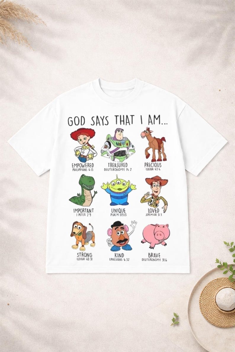 May include: White t-shirt featuring cartoon characters with the text "GOD SAYS THAT I AM...". Each character has a corresponding word like "Empowered" and a Bible verse reference. The shirt has a crew neck and short sleeves.