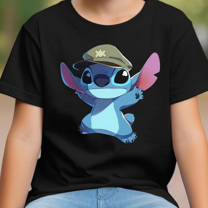 May include: A black t-shirt featuring a graphic print of a blue alien character with large ears wearing a tan military-style cap with a light-colored cross emblem on the front. The character is depicted with arms outstretched in a dynamic pose.