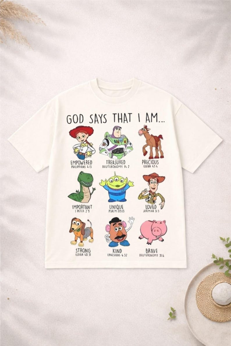 May include: Off-white t-shirt featuring cartoon characters with the text "GOD SAYS THAT I AM..." and various positive affirmations. The shirt includes characters like Woody, Buzz Lightyear, and others, with corresponding Bible verses.