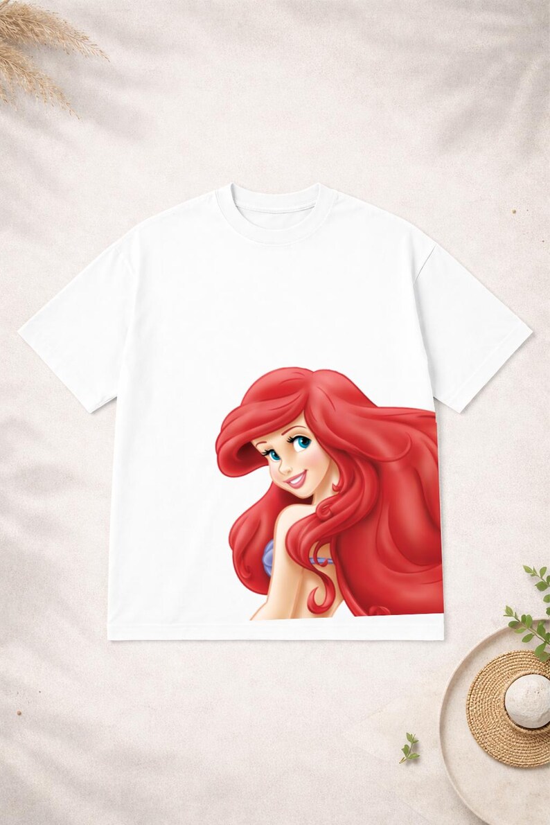 Puede incluir: Camiseta blanca con una ilustraci&oacute;n de dibujos animados de un personaje con pelo largo rojo y ojos azules. El personaje est&aacute; sonriendo. La camiseta est&aacute; hecha de un material suave y c&oacute;modo.