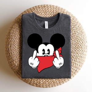 May include: Dark gray t-shirt featuring a cartoon mouse with black ears, white gloves, and a red bandana. The mouse is giving the middle finger with both hands. The shirt is made of a soft material.