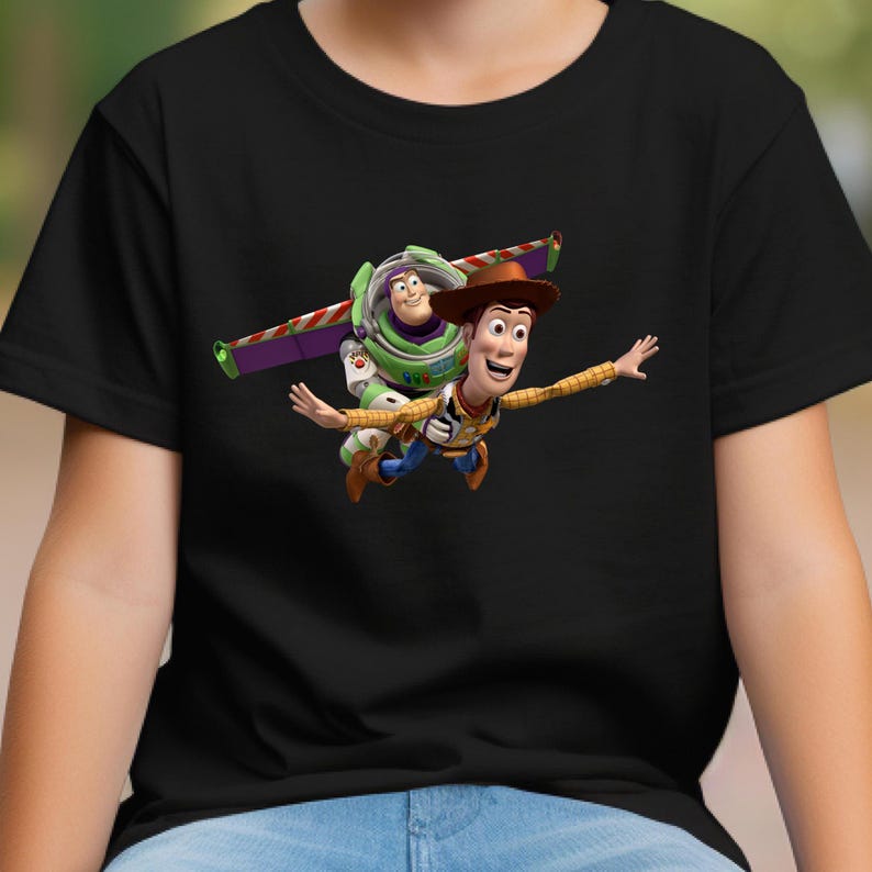 May include: Black t-shirt featuring a colorful graphic of Woody and Buzz Lightyear from Toy Story. Woody is wearing a cowboy hat and Buzz has his wings extended. The design is vibrant and detailed.