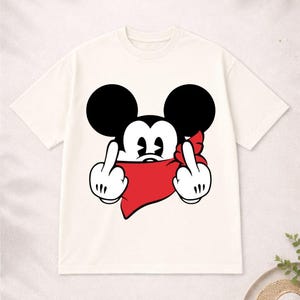 May include: Cream-colored t-shirt featuring a cartoon mouse character with black ears and a red bandana. The mouse is giving the middle finger with both hands. A humorous graphic tee.