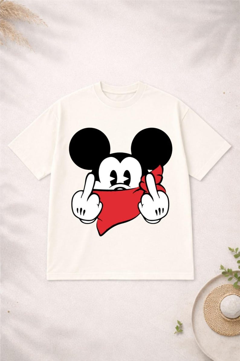 May include: Cream-colored t-shirt featuring a cartoon mouse character with black ears and a red bandana. The mouse is giving the middle finger with both hands. A humorous graphic tee.