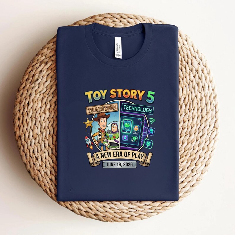 May include: Navy blue t-shirt featuring a colorful graphic for "Toy Story 5." The design includes Woody and Buzz Lightyear, a tablet with app icons, and the text "A New Era of Play, June 19, 2026."