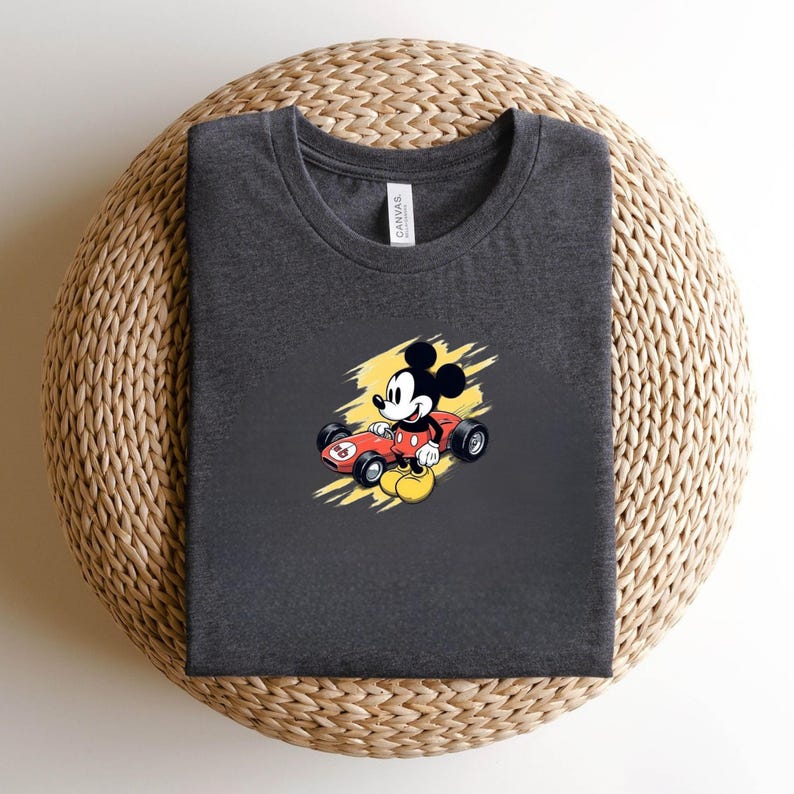 May include: Dark grey t-shirt with a cartoon Mickey Mouse design in a red racing car with yellow accents. The shirt has a crew neck and is made of a soft material. The image of Mickey Mouse is in the centre of the t-shirt.