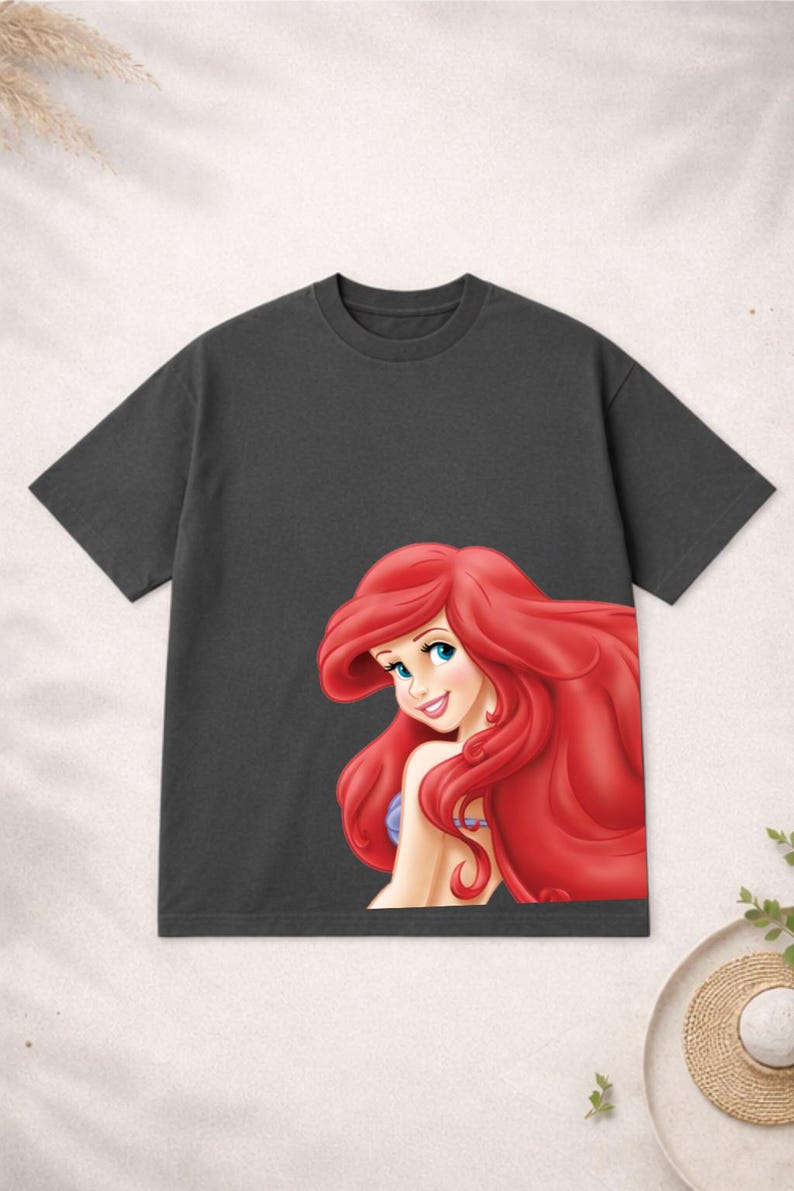 Puede incluir: Camiseta gris oscuro con una ilustraci&oacute;n de dibujos animados de una sirena con pelo rojo, ojos azules y un collar morado. El gr&aacute;fico est&aacute; en la parte delantera de la camiseta.