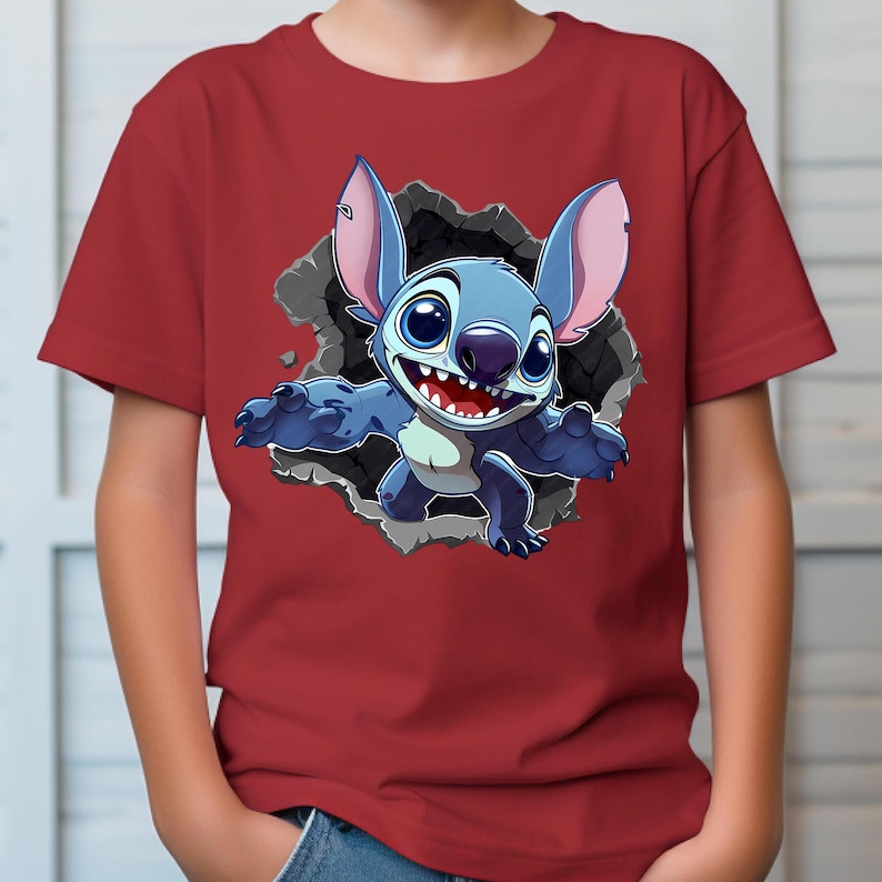 May include: A red t-shirt with a cartoon image of Stitch, a blue alien, breaking through a wall. Stitch has large ears and a wide grin. The graphic is detailed with shading and highlights, creating a 3D effect.