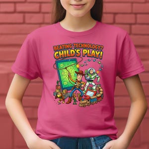 May include: A pink t-shirt featuring a colorful graphic of cartoon characters, including a cowboy and a space ranger, with the text "BEATING TECHNOLOGY? CHILD'S PLAY!". The design includes a dog, a train, and a broken screen.