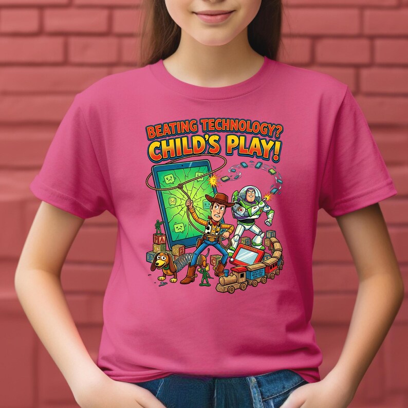 May include: A pink t-shirt featuring a colorful graphic of cartoon characters, including a cowboy and a space ranger, with the text "BEATING TECHNOLOGY? CHILD'S PLAY!". The design includes a dog, a train, and a broken screen.