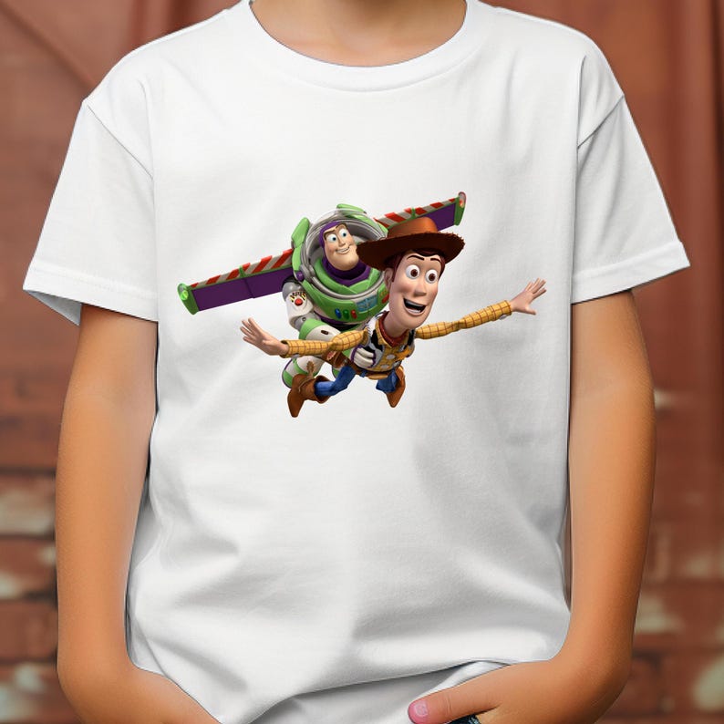 May include: White t-shirt featuring a colorful graphic of Woody and Buzz Lightyear from Toy Story. Woody is wearing a cowboy hat and Buzz Lightyear has his wings extended. The design is centered on the front of the shirt.