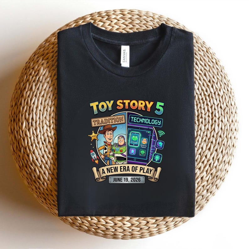 May include: Black t-shirt featuring a colorful graphic for "Toy Story 5." The design includes Woody and Buzz Lightyear, a rocket, and a tablet with app icons. Text reads "Tradition Technology" and "A New Era of Play, June 19, 2026."