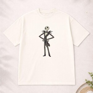 Puede incluir: Camiseta de color crema con una ilustraci&oacute;n en blanco y negro de Jack Skellington. El personaje est&aacute; representado con su traje a rayas, con los brazos en jarras. La camiseta tiene cuello redondo y mangas cortas, inspirada en Pesadilla antes de Navidad.
