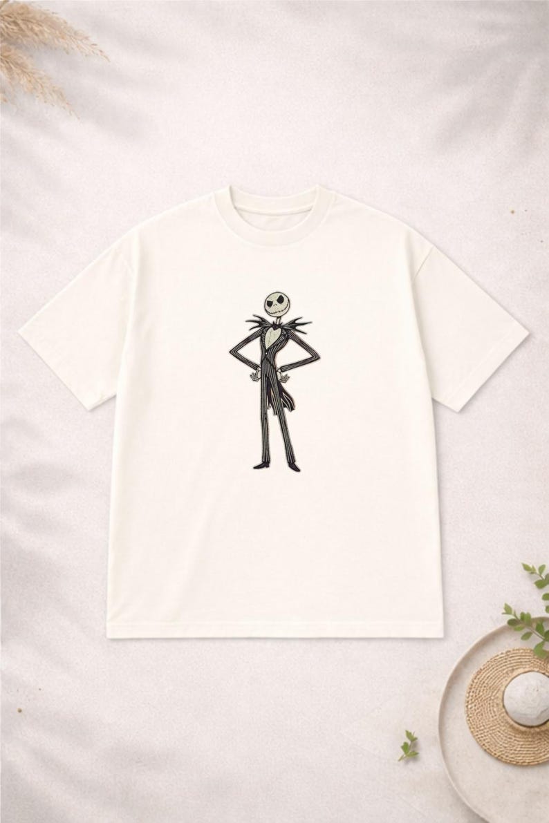 Puede incluir: Camiseta de color crema con una ilustraci&oacute;n en blanco y negro de Jack Skellington. El personaje est&aacute; representado con su traje a rayas, con los brazos en jarras. La camiseta tiene cuello redondo y mangas cortas, inspirada en Pesadilla antes de Navidad.