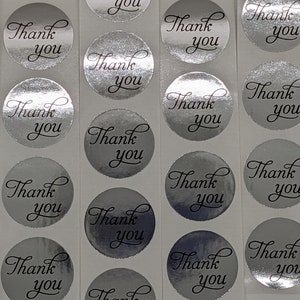 May include: Roll of silver thank you stickers with a black cursive font. Each sticker is round and has the words "Thank You" written on it.