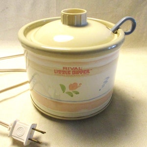 May include: A white Rival Little Dipper electric stoneware server with a pink and blue floral design. The server has a lid and a small spoon.