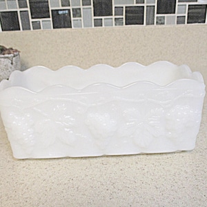 May include: White milk glass planter with a scalloped edge and a floral design. The planter is made of opaque white glass and has a rectangular shape.