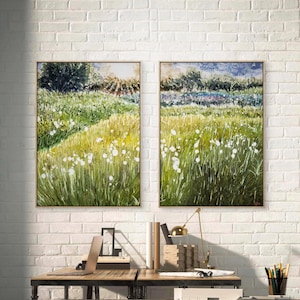 Könnte beinhalten: Zwei gerahmte Landschaftsbilder, die ein Feld mit hohem, grünem Gras und weißen Blumen zeigen. Die Gemälde haben einen goldenen Rahmen und hängen an einer weißen Backsteinmauer. Die Gemälde befinden sich über einem Holzschreibtisch mit Laptop und Schreibtischzubehör.