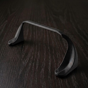May include: A black, curved object with a bridge-like design. The object has a textured surface and appears to be made of a matte material. The shape suggests it could be a handle or support for another item.