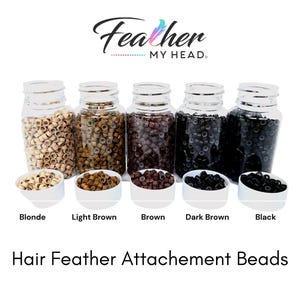 Peut inclure: Cinq pots en plastique transparent remplis de petites perles rondes de différentes couleurs : blond, brun clair, brun, brun foncé et noir. Les pots sont étiquetés avec la couleur de cheveux correspondante. Le texte "Feather MY HEAD." est en haut de l’image. Le texte "Hair Feather Attachement Beads" est en bas de l’image.