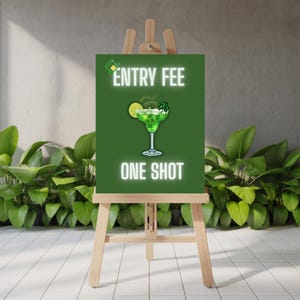 May include: A green sign on a wooden easel with the words "ENTRY FEE" and "ONE SHOT" in white neon-style lettering. A green cocktail with a lime slice is in the center. The sign is in front of green plants.